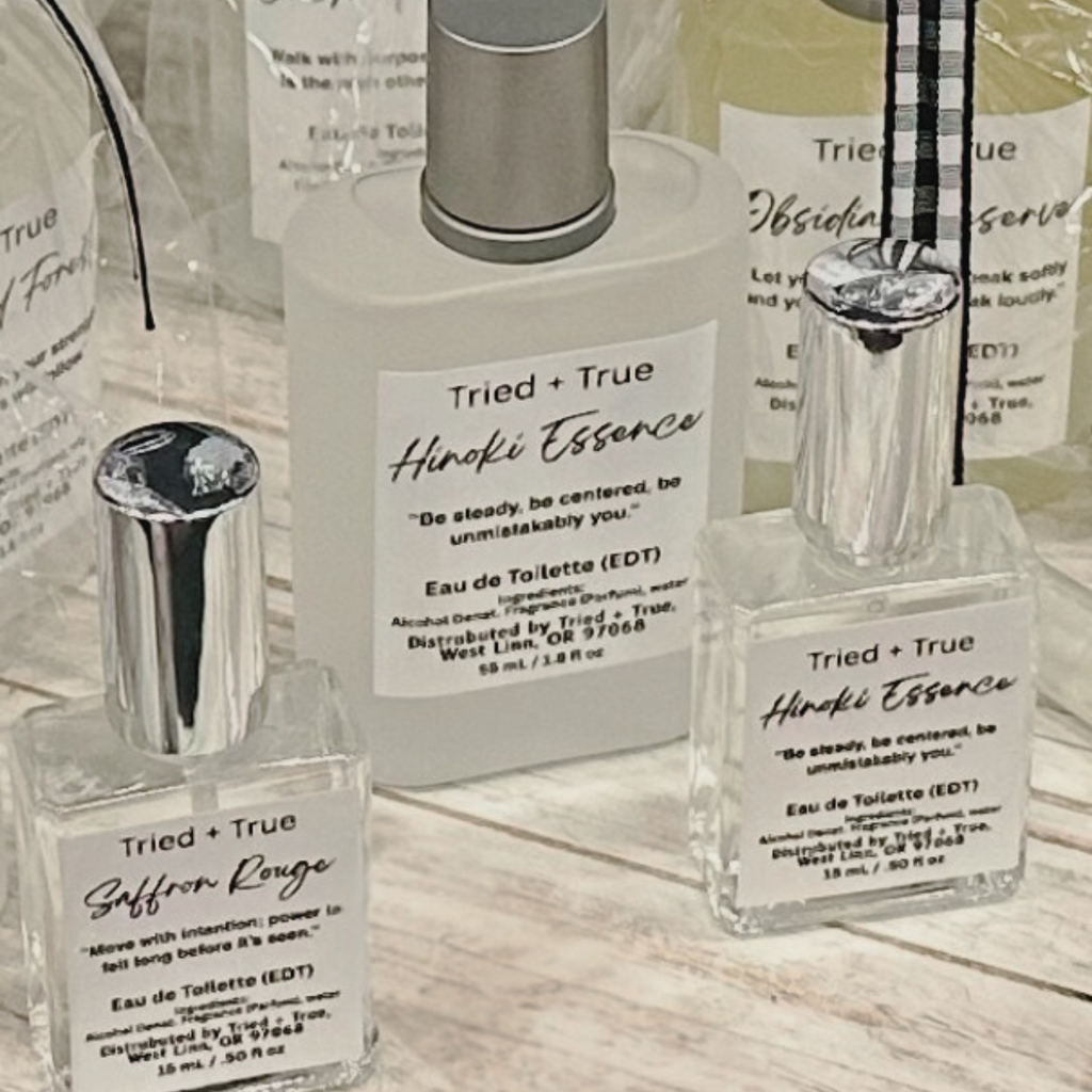 Three Tried + True perfume bottles, including Hinoki Essence and Saffron Rouge, displayed on a wooden surface.